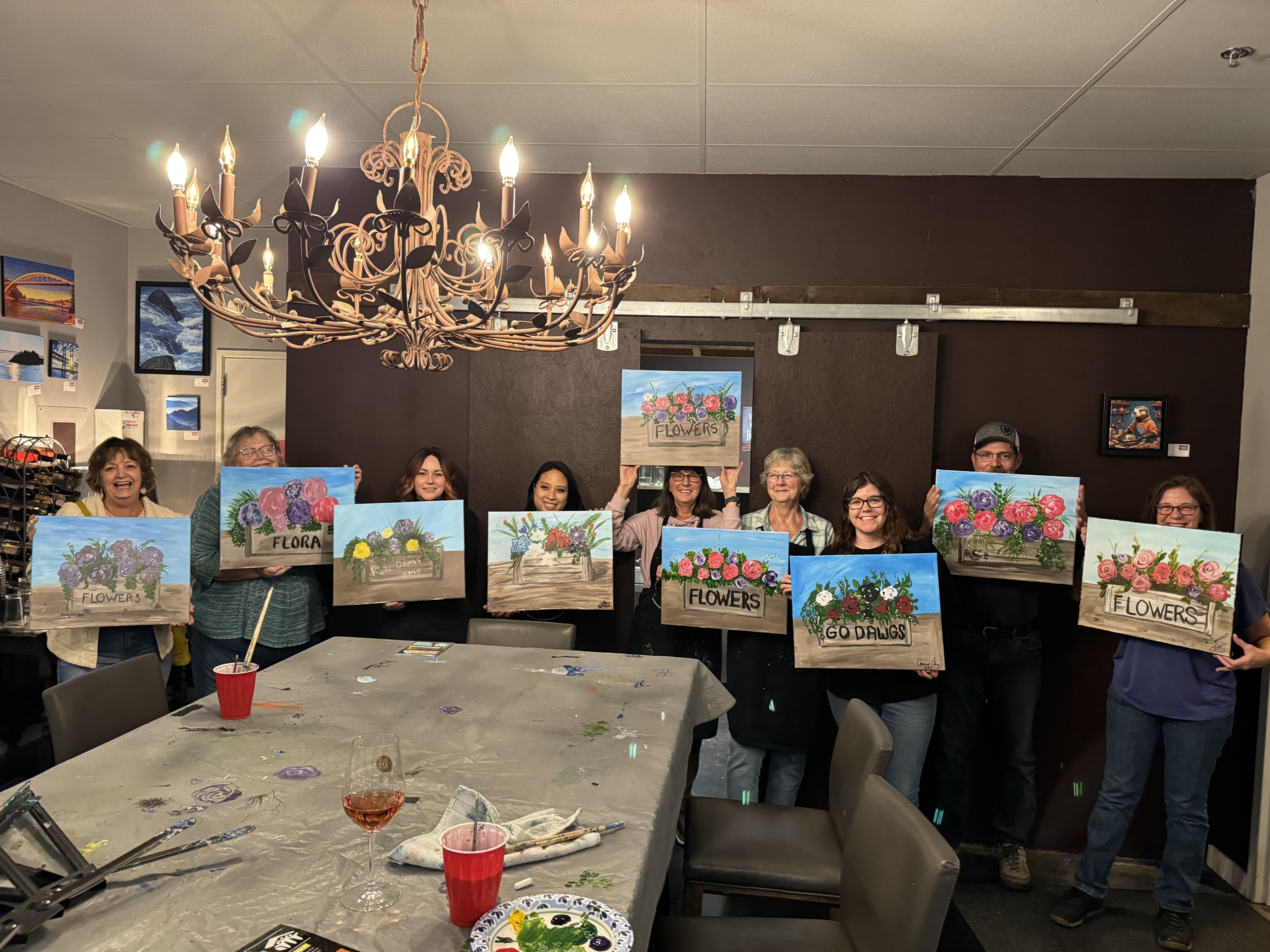 group standing inside holding paintings of a box of flowers as part of a skagit habitat for humanity fundraiser with the speckled hen paint parties