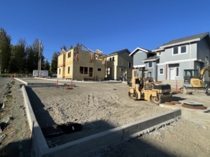 full view of four duplexes being built by Skagit Habitat for Humanity in Anacortes. Two finished duplexes to the right of the image and one unfinished building on the left with machinery in the middle.