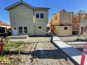 Skagit Habitat for Humanity's 8-home project in Anacortes WA. Finished concrete, with one finished building to the left and one framed building on the right.