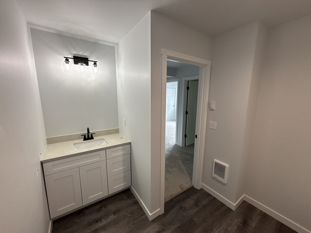 Finished bathroom at Skagit Habitat for Humanity's 8-home construction project in Anacortes, Washington. A small bathroom with a lightly colored bathroom vanity and sink and lights above it facing the door looking into the hallway of the upstairs.