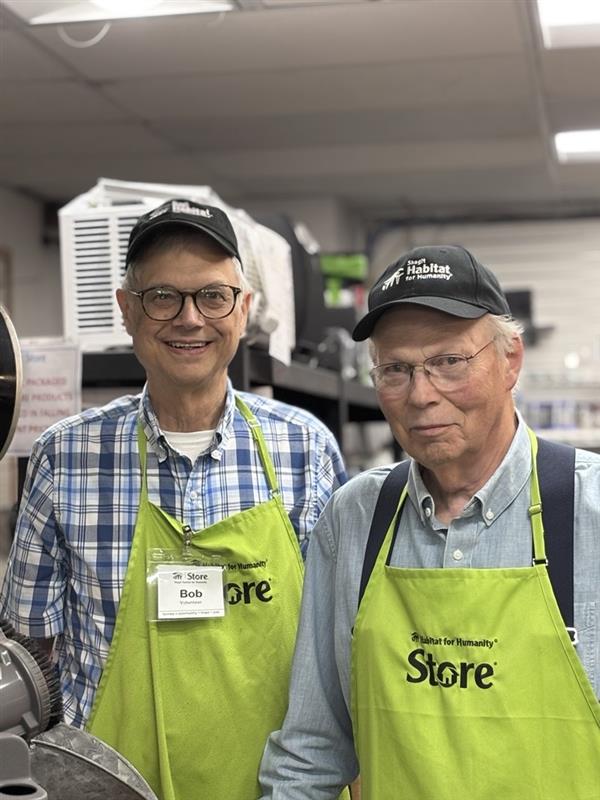 two Skagit Habitat for Humanity Store volunteers in green aprons standing next to each other smiling.