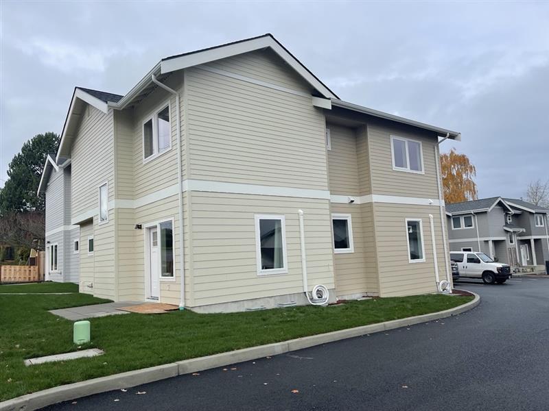 Skagit Habitat for Humanity homes in Anacortes Washington. The duplex is tan and brown with other duplexes in the background. Green grass surrounds the home.