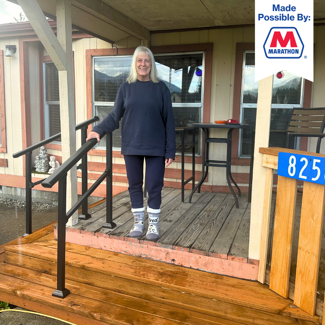 Denise standing on her newly repaired deck and stairs complete with black handrails through Skagit Habitat for Humanity's Critical Repair Program.