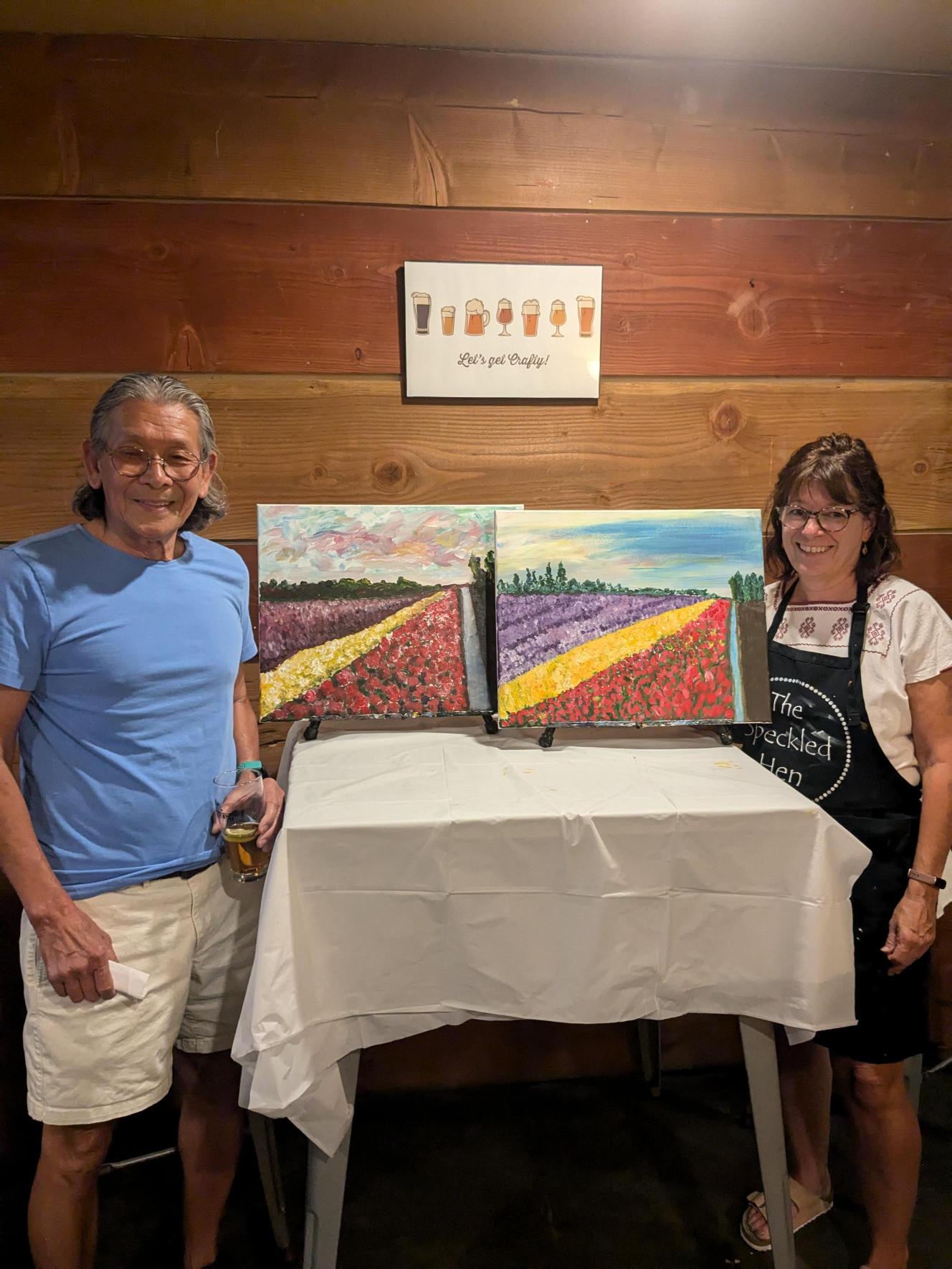 two people standing next to their paintings at a Speckled Hen Paint n Sip fundraiser event for Skagit Habitat for Humanity